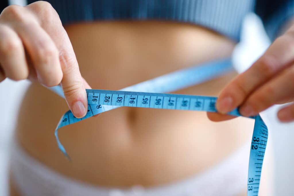 Nő kék mérőszalaggal méri a derékbőségét a fogyasztó injekciók hatásának nyomon követéséhez.